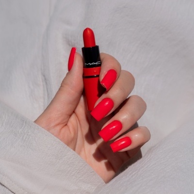 Batom vermelho MAC em mão com unhas vermelhas sobre tecido branco