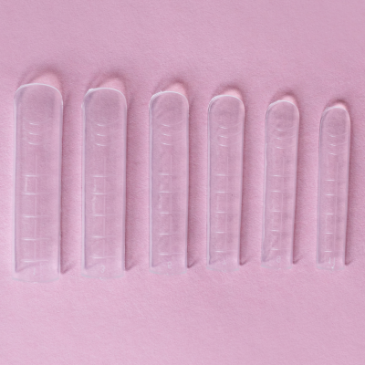 Sete capas de unhas transparentes em fila sobre fundo rosa