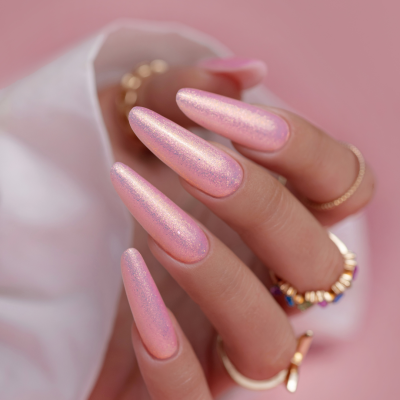 Unhas compridas com verniz rosa cintilante e anéis dourados coloridos em fundo rosa