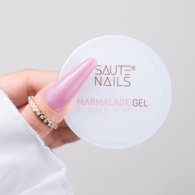Frasco branco de gel para unhas SAUTE NAILS Marmalade Gel Bubble Gum segurado por mão com unhas rosas e anéis.