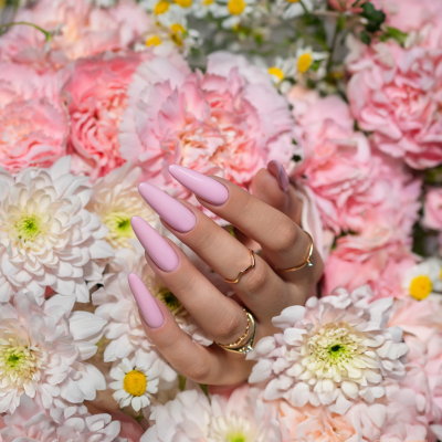 Mãos femininas com unhas rosa claro entre flores rosas, brancas e amarelas