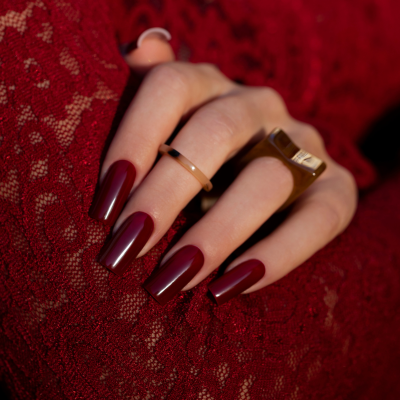 Mão com unhas vermelhas longas e anéis sobre tecido rendado vermelho