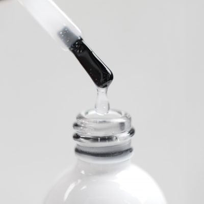 Frasco aberto de verniz para unhas com conta-gotas borrifando líquido transparente e logo SAUTE NAILS