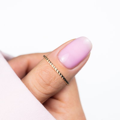 Close-up de dedo com unha rosa e anel dourado fino