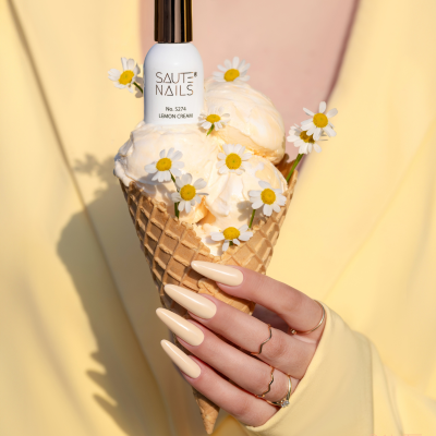 Verniz de unhas SAUTE NAILS numa casquinha de gelado com chantilly e flores, mão com unhas creme e anéis