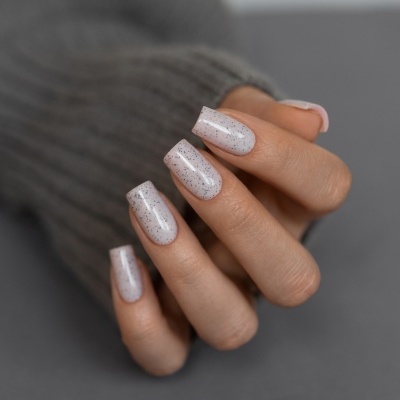 Mão com unhas compridas pintadas de verniz branco com pontos pretos sobre fundo cinzento.