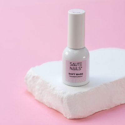 Frasco de verniz SAUTE NAILS SOFT BASE TRANSPARENT sobre bloco branco e fundo rosa