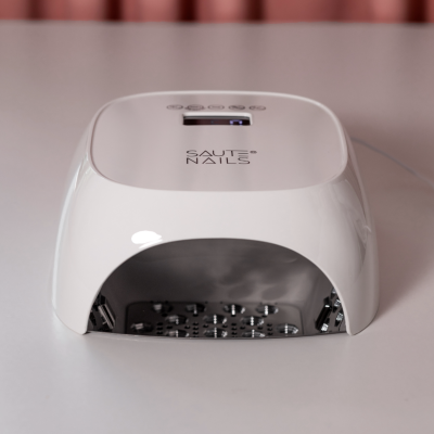 Secador de unhas LED branco SAUTE NAILS em superfície branca.