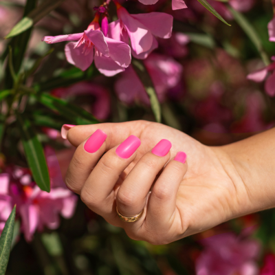 Mão com unhas rosa fosca perto de flores cor-de-rosa