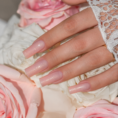 Unhas postiças rosa claro com verniz cintilante entre flores e renda branca