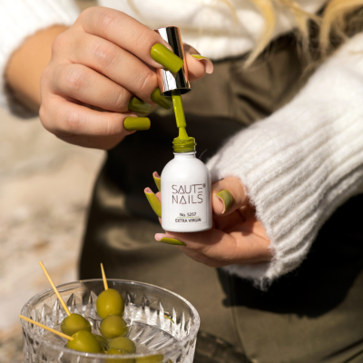 Verniz para unhas verde SAUTE NAILS com mão feminina e azeitonas verdes em tigela de vidro
