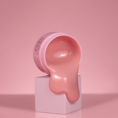 Frasco rosa de creme ou gel a transbordar sobre cubo branco em fundo rosa.