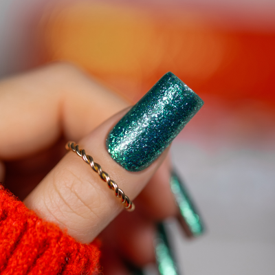 Unha artificial verde brilhante com brilhos no dedo com anel dourado e suéter vermelho