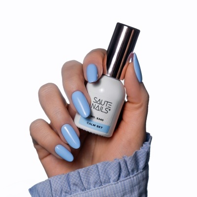 Mão com unhas azuis segurando frasco de verniz SAUTE NAILS calm sky