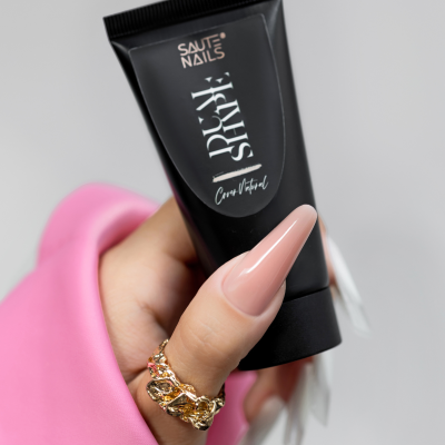 Mão com unhas longas nude segurando tubo preto de produto SAUTE NAILS