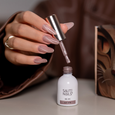 Frasco branco de verniz de unhas Saute Nails com pincel e unhas compridas rosa.