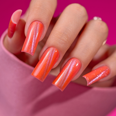 Unhas falsas laranja cintilantes em mão com fundo rosa e texto SAUTE NAILS