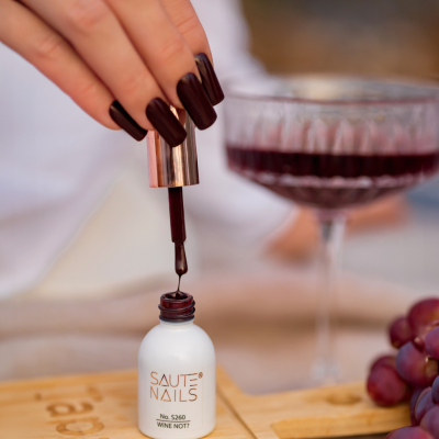 Frasco com verniz para unhas vinho SAUTE NAILS ao lado de taça de vinho e uvas