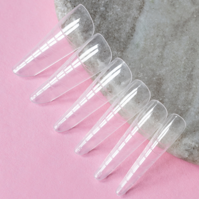 Seis unhas postiças transparentes sobre pedra cinza com fundo rosa