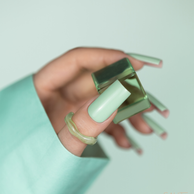 Mão com unhas verdes menta segurando um bloco verde transparente