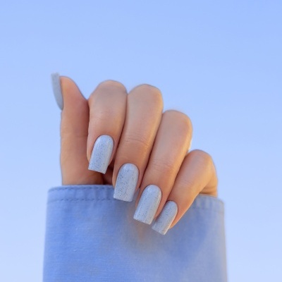 Mão com unhas azul claro manchadas, manga azul e céu azul de fundo