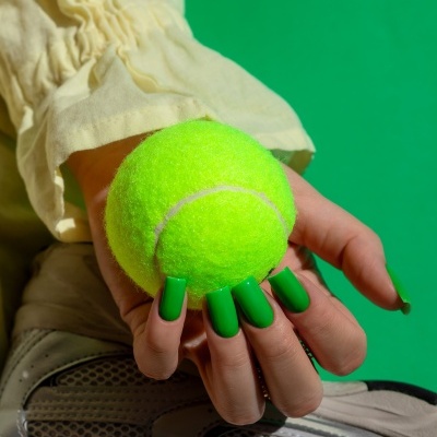 Mão segura bola de ténis sobre ténis cinzento com fundo verde