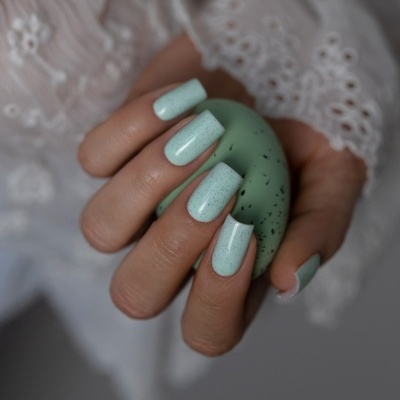 Unhas pintadas de azul claro com pontos pretos segurando ovo verde com manchas pretas