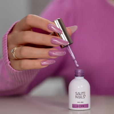Frasco de verniz Saute Nails nº E12 Cat Eyes lilás com brilho e mão feminina a pintar unhas cor rosa