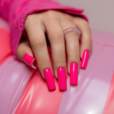 Mão com unhas artificiais fúcsia em balão cor-de-rosa com texto SAUTE NAILS®