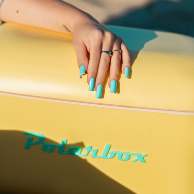 Mão com unhas azuis segurar mala amarela Polarbox
