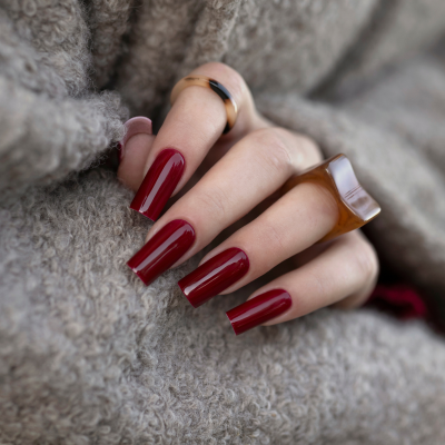 Unhas vermelhas longas com anéis castanhos em fundo cinzento.