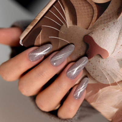 Unhas artificiais cinzentas com glitter prateado em formato almendrado segurando caixa com ilustração artística