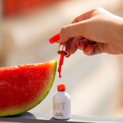 Frasco de verniz de unhas branco com pincel vermelho perto de fatia de melancia