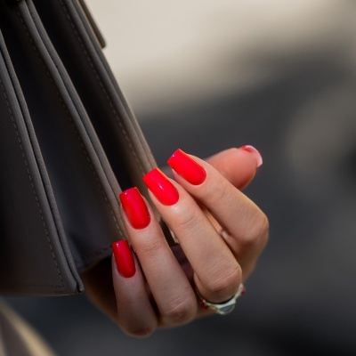 Mãos com unhas vermelhas seguram alça de bolsa cinzenta com detalhes metálicos