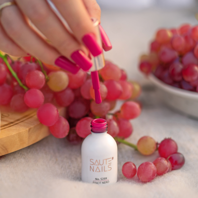 Esmalte de unhas rosa da SAUTE NAILS com uvas vermelhas ao fundo