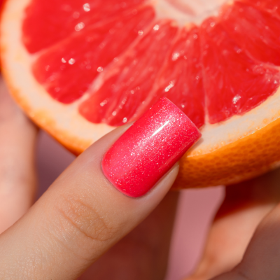 Unha com verniz rosa brilhante segurando meio toranja vermelha