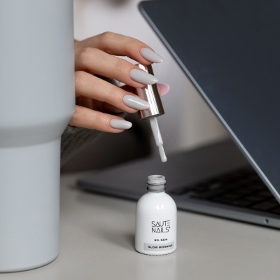 Frasco verniz unhas branco SAUTE NAILS S339 SLOW MORNING com pincel e mão com unhas pintadas cinza claro
