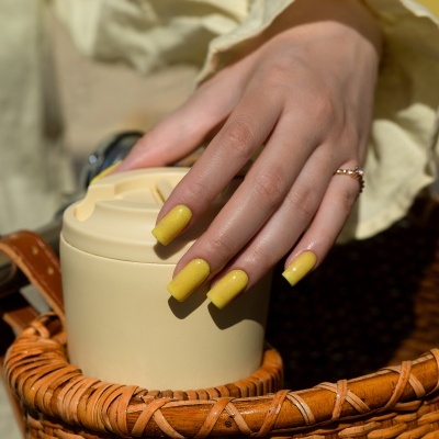 Mão com unhas amarelas segurando recipiente bege dentro de cesta de vime