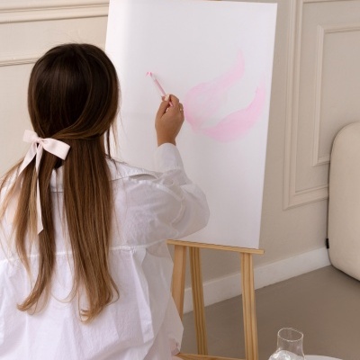 Mulher pintando tela em cavalete com tinta rosa