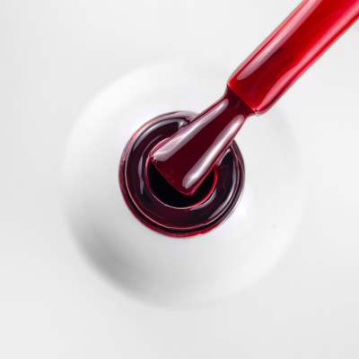 Frasco branco de verniz de unhas com pincel a aplicar verniz vermelho escuro