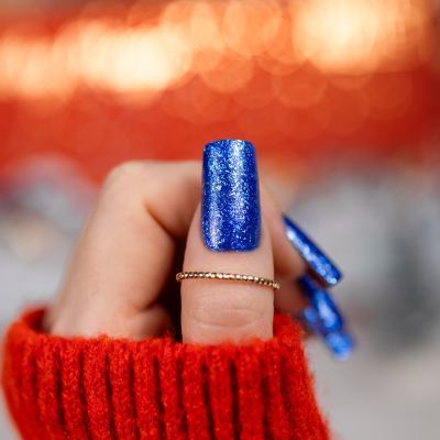 Unha artificial longa azul glitter em mão com anel dourado e malha vermelha