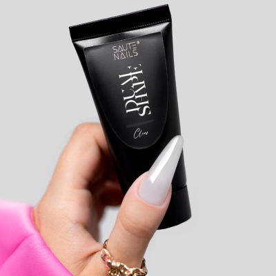 Mão feminina com unha branca segurando tubo preto de cosmético Saute Nails