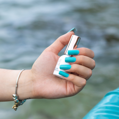 Mão com unhas azuis segurando frasco de verniz de unhas junto a água