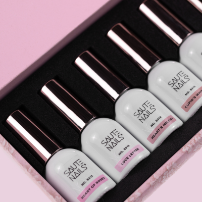 Conjunto de vernizes SAUTE NAILS em embalagem rosa e interior preto, cinco frascos brancos com tampa prateada e etiquetas com nomes distintos.
