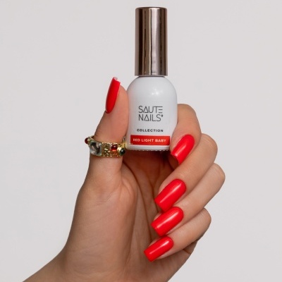 Mão segurando frasco de verniz SAUTE NAILS com unhas vermelhas