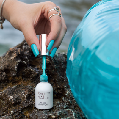 Frasco branco de verniz de unhas SAUTE NAILS número 5252 CELEBRITY LOOK com tampa prateada e mão com unhas azuis.