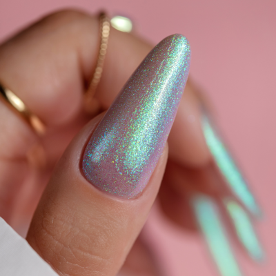 Unhas holográficas azuis com reflexos verdes e roxos em fundo rosa com texto SAUTE NAILS®.