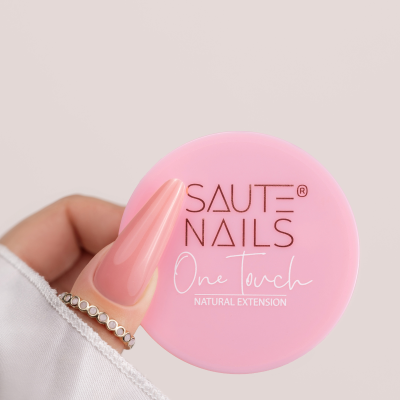 Recipiente rosa SAUTE NAILS One Touch NATURAL EXTENSION segurado por mão com unhas compridas cor-de-rosa e pulseira