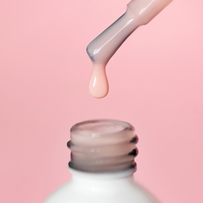 Frasco branco de verniz de unhas com pincel a gotejar verniz nude e fundo rosa