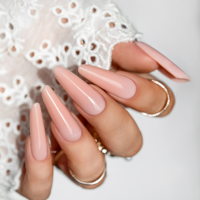 Mãos com unhas longas nude e anéis prateados, com manga branca recortada e logo SAUTE NAILS
